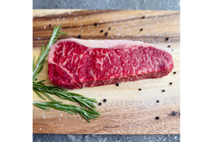 Raw steak on a wooden cutting board with rosemary and peppercorns