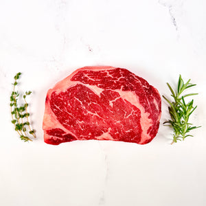 Raw steak with herbs on a white background. 14 oz Ribeye by Zion Farms.