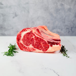 Raw rib roast on a marble surface with thyme sprigs, against a gray background