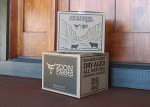Two cardboard boxes from Zion Farms in front of a wooden door.