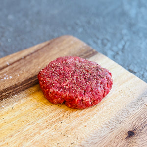Raw hamburger patty on a wooden cutting board with a blurred background