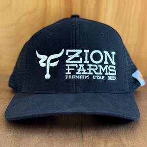 Black cap with 'Zion Farms Premium Utah Beef' logo on a wooden surface